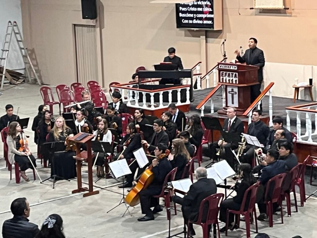 A 30+ member orchestra sits in the church auditorium with their instruments in concert.