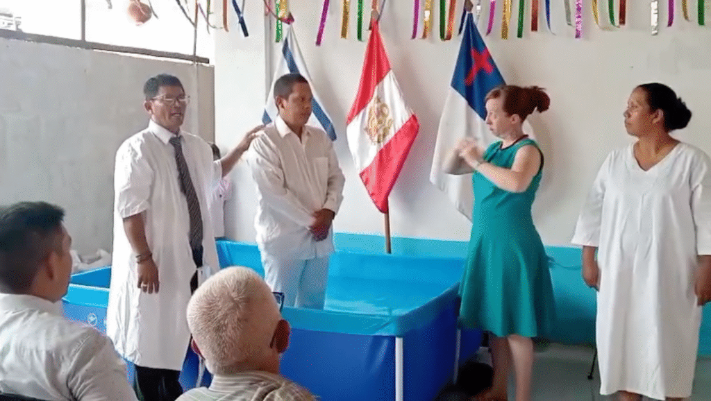 A deaf convert stands in a baptismal pool near the pastor and an interpreter, ready for baptism.